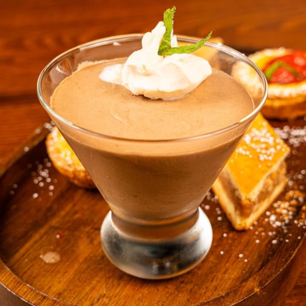 Peggy's chocolate mousse with whipped cream and mint, surrounded by pastries on a wooden tray.