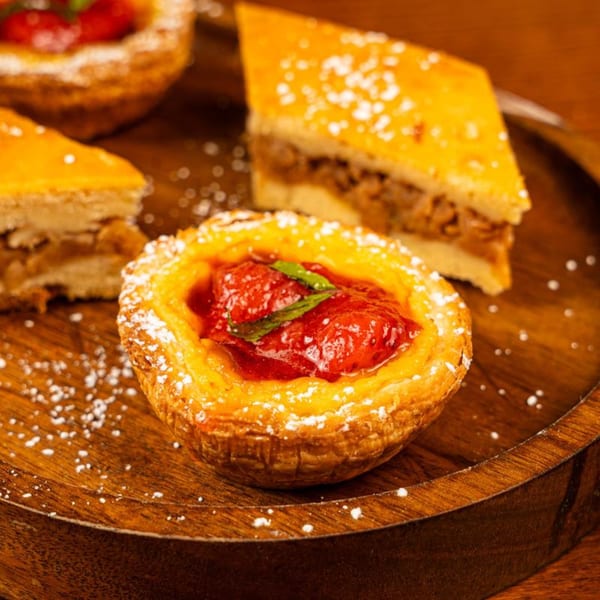 A strawberry tart with mint and powdered sugar, alongside two baklava slices on a wooden tray.
