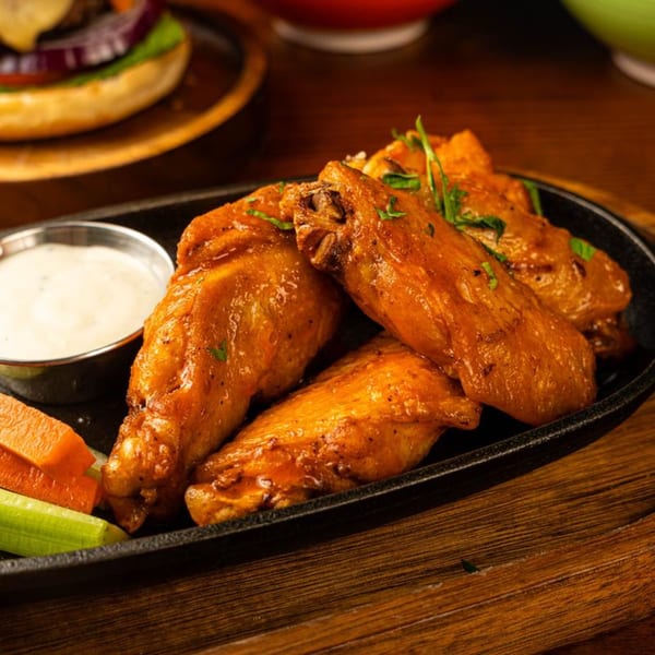 Crispy Peggy's chicken wings with ranch dip, carrots, and celery on a black plate.