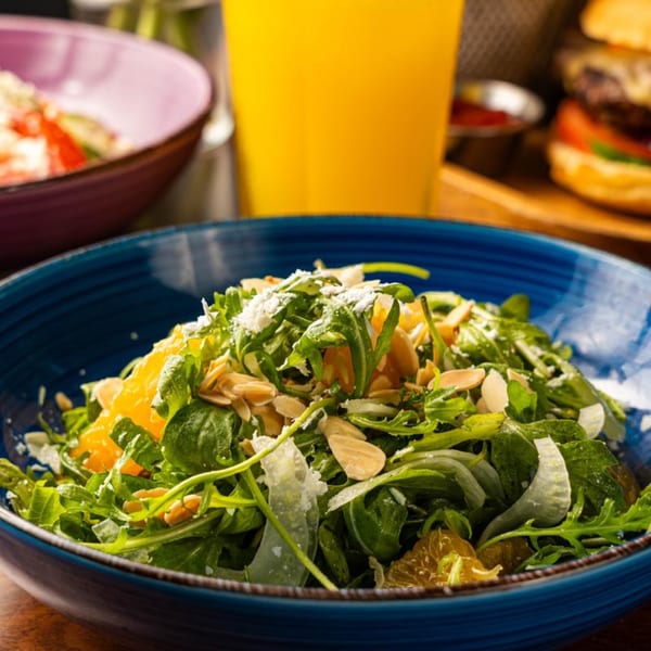 Arugula salad with orange segments, sliced almonds, and parmesan cheese in a blue bowl.