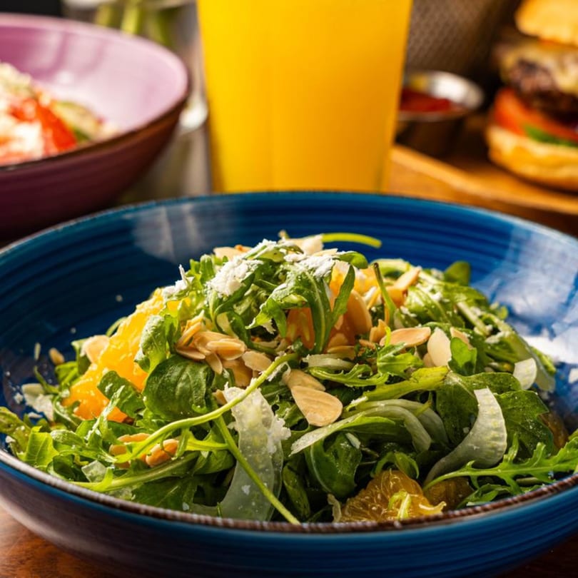 Arugula salad with orange segments, sliced almonds, and parmesan cheese in a blue bowl.