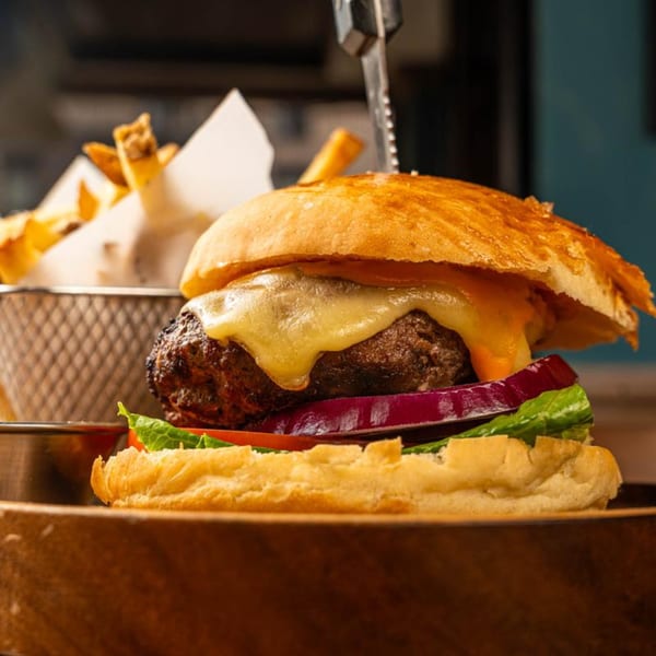 A Peggy's cheeseburger with lettuce, tomato, and red onion, served with fries.