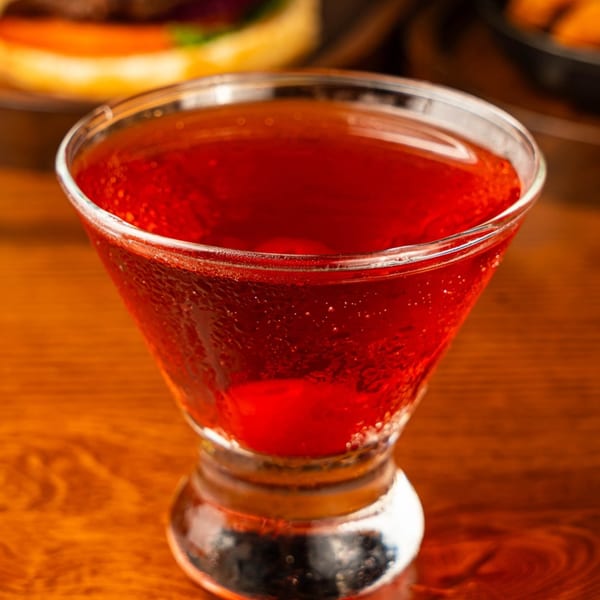 Close-up of a vibrant red cocktail in a stemmed glass on a wooden table at Peggy's.