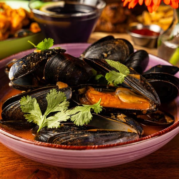 Steamed mussels in a rich red broth, garnished with fresh cilantro, served in a purple bowl.