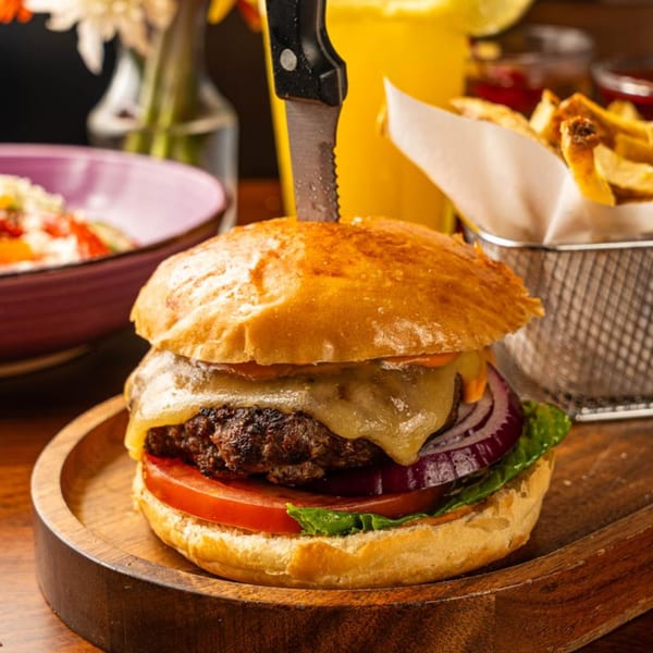 A Peggy's burger with melted cheese, tomato, onion, and lettuce, served with fries and a drink.