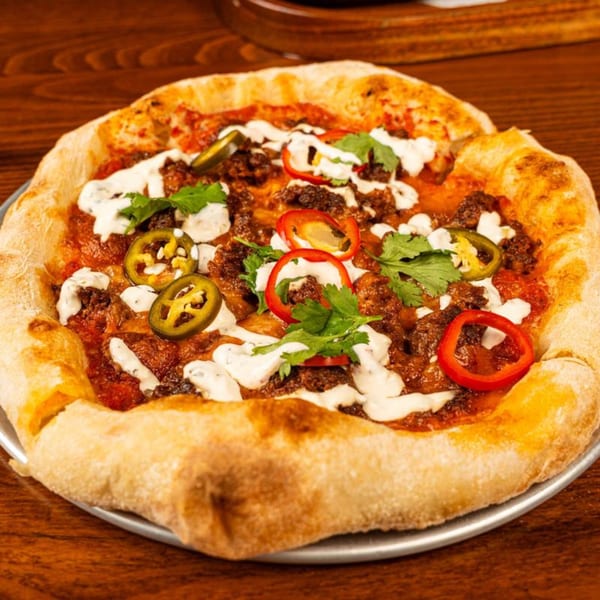 A European-style pizza from Peggy's, topped with meat, red peppers, jalapeños, and white sauce.